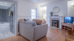 A modern living room with a grey sofa, a fireplace, a TV, and a wooden floor. - Ivy Cellar - 1 Bedroom Apartment - Tenby (Tenby)