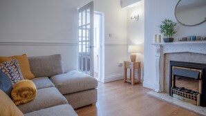 A living room with a sofa, a fireplace, and a door leading to another room. - Ivy Cellar - 1 Bedroom Apartment - Tenby (Tenby)