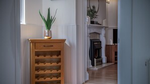 A wooden wine rack with multiple slots, a potted plant, and a fireplace in the background. - Ivy Cellar - 1 Bedroom Apartment - Tenby (Tenby)