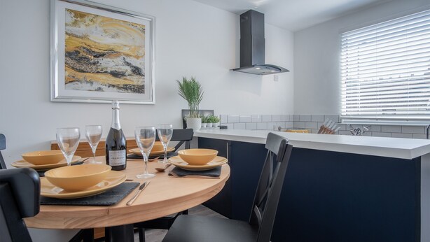 A modern kitchen with a round dining table, black chairs, and a central island. - Ivy Cellar - 1 Bedroom Apartment - Tenby (Tenby)