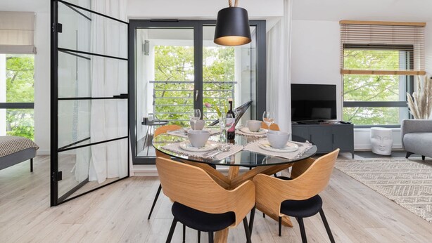 A modern dining area with a glass table, wooden chairs, and a black pendant light.