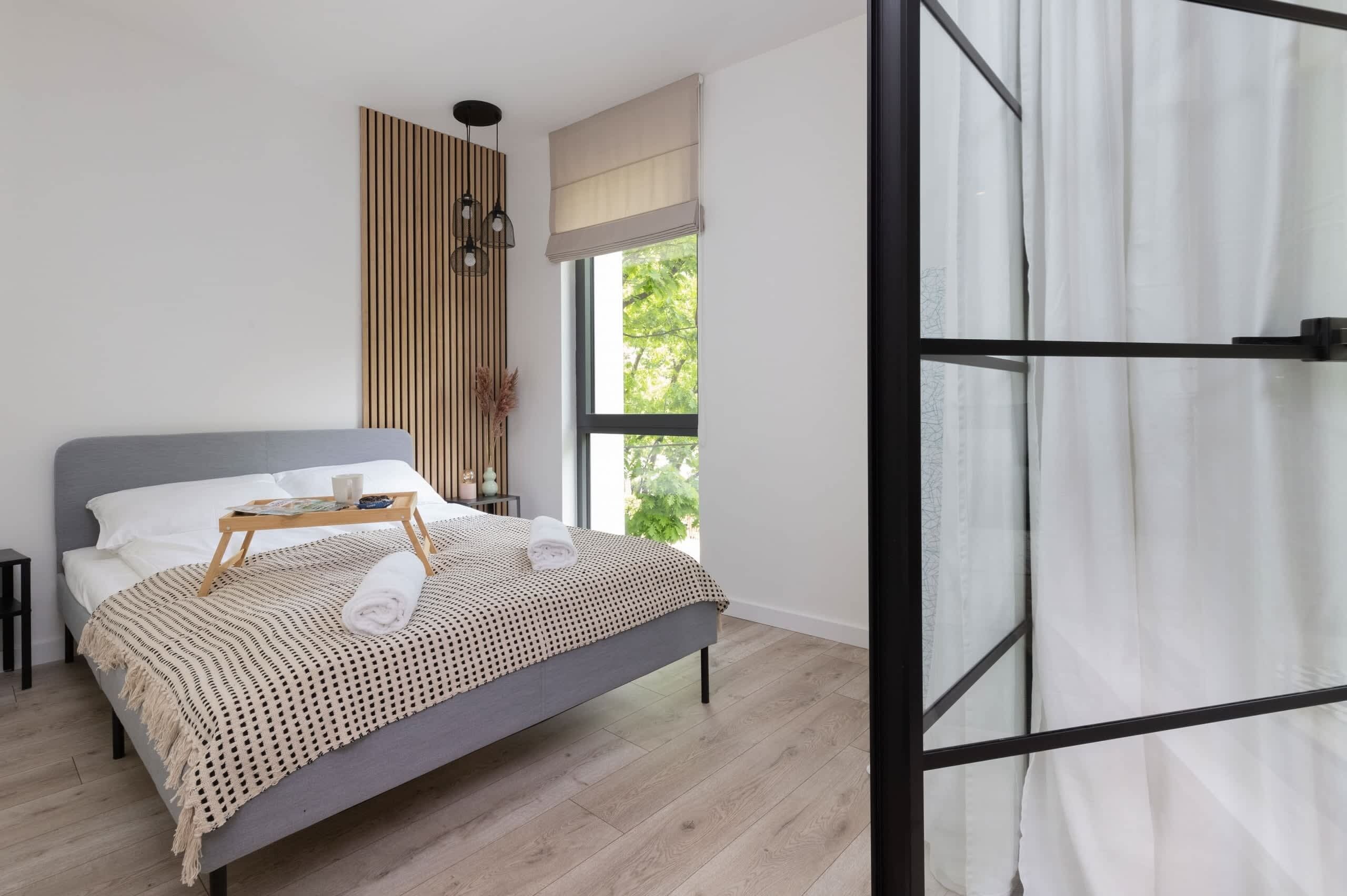 A modern bedroom with a grey bed, wooden headboard, and a bedside table with a tray.