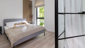 A modern bedroom with a grey bed, wooden headboard, and a bedside table with a tray.