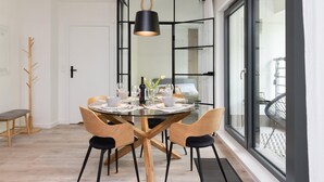 A modern dining area with a glass table, wooden chairs, and a black pendant light.