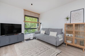 A modern living room with a grey sofa, a flat-screen TV, a wooden cabinet with glassware, and a framed artwork on the wall.