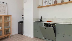 A modern kitchen with a built-in dishwasher, a wooden cabinet with glassware, and a marble countertop.