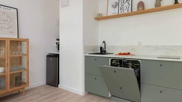 A modern kitchen with a built-in dishwasher, a wooden cabinet with glassware, and a marble countertop.