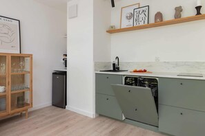 A modern kitchen with a built-in dishwasher, a wooden cabinet with glassware, and a marble countertop.