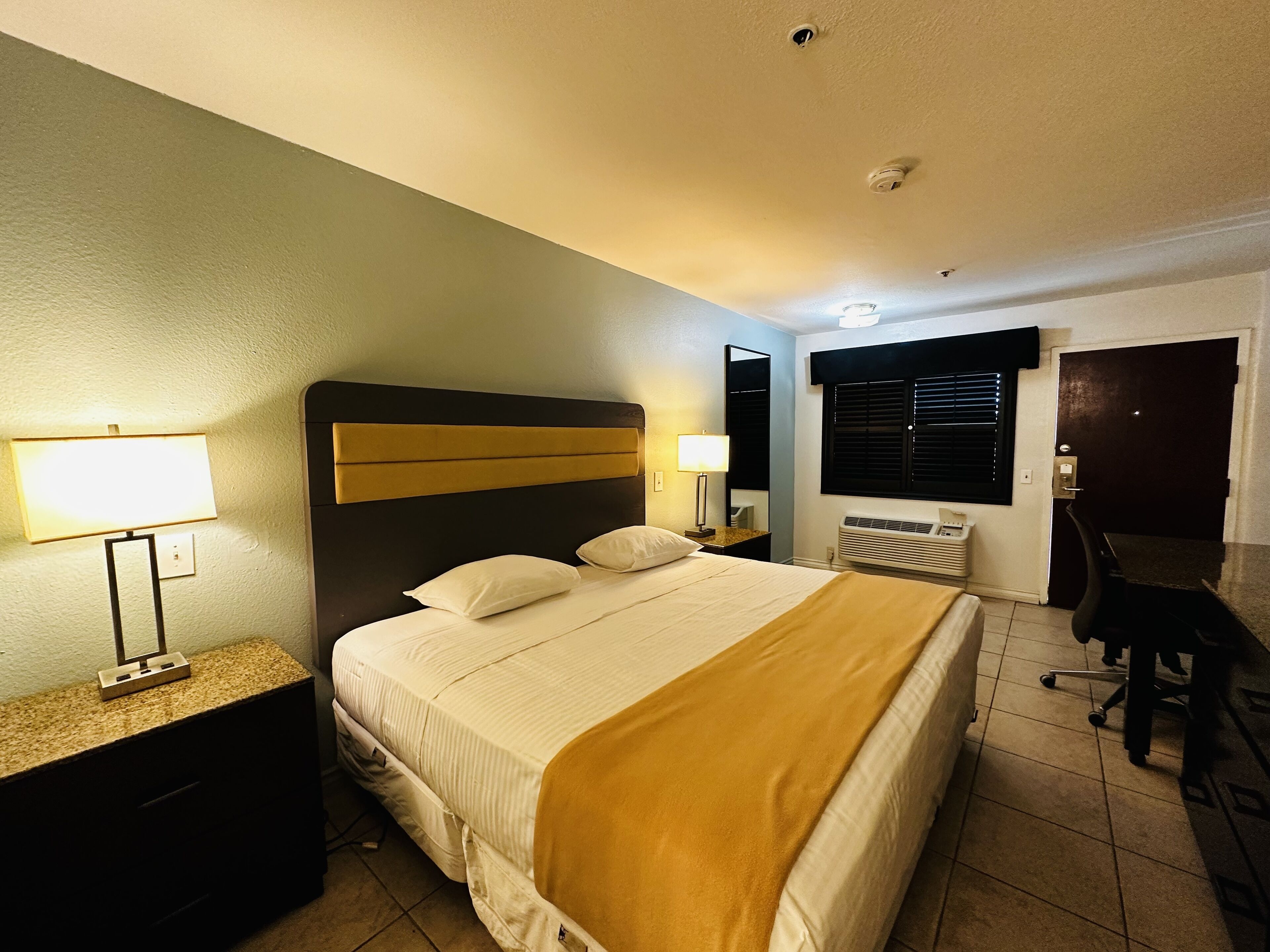 A hotel room with a bed, bedside lamps, a desk, and a chair.
