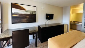 A hotel room with a bed, a desk with a chair, a television, and a painting on the wall. - Casa Blanca Express & Suites Cypress Buena Park - Anaheim Area (Cypress)