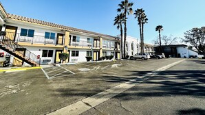 A multi-story motel with a parking lot, palm trees, and a clear blue sky. - Casa Blanca Express & Suites Cypress Buena Park - Anaheim Area (Cypress)