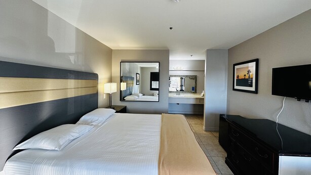 A hotel room with a large bed, a dresser, a TV, a mirror, and a bathroom visible through an open door. - Casa Blanca Express & Suites Cypress Buena Park - Anaheim Area (Cypress)