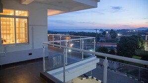 A modern hotel room with a balcony overlooking a cityscape at dusk. - LUXE-3BEDROOM CONDO WITH LAKE AND GOLF COURSE VIEWS (Kampala)