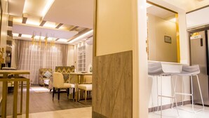A modern living room with a dining area, a kitchen with bar stools, and a wooden accent wall. - LUXE-3BEDROOM CONDO WITH LAKE AND GOLF COURSE VIEWS (Kampala)