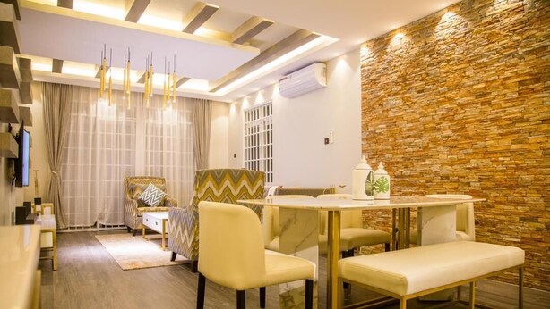 A modern dining area with a stone wall, a chandelier, and a dining table with chairs. - LUXE-3BEDROOM CONDO WITH LAKE AND GOLF COURSE VIEWS (Kampala)