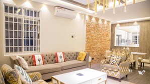 A modern living room with a beige sofa, patterned armchair, and a white coffee table. - LUXE-3BEDROOM CONDO WITH LAKE AND GOLF COURSE VIEWS (Kampala)