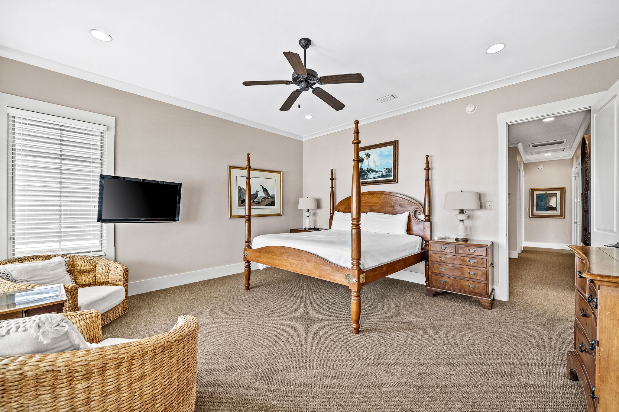 A bedroom with a four-poster bed, a television mounted on the wall, and a wicker chair.