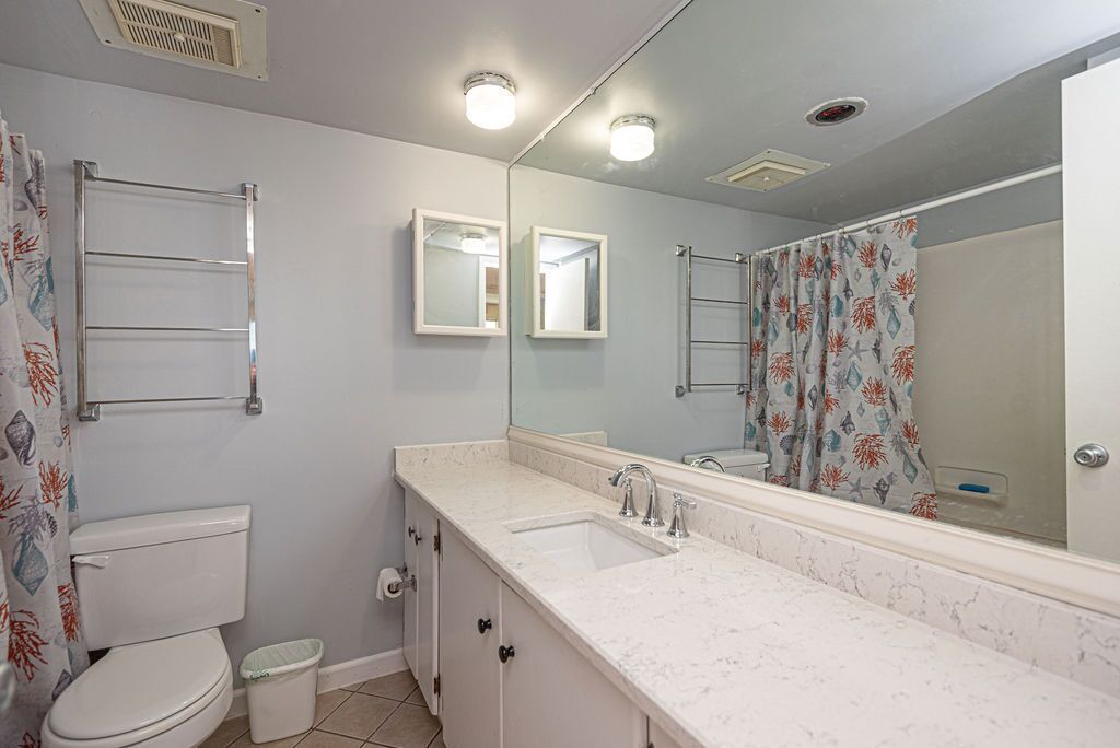 Een badkamer met een wit toilet, een wastafel met spiegel erboven, een handdoekhouder en een douchegordijn met bladmotief.