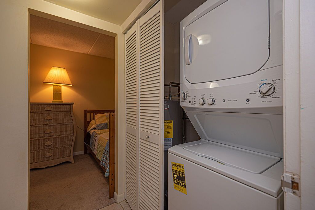 Ein Waschraum mit einer Waschmaschine und einem Trockner, einem Holzschrank und einem Bett mit Lampe.