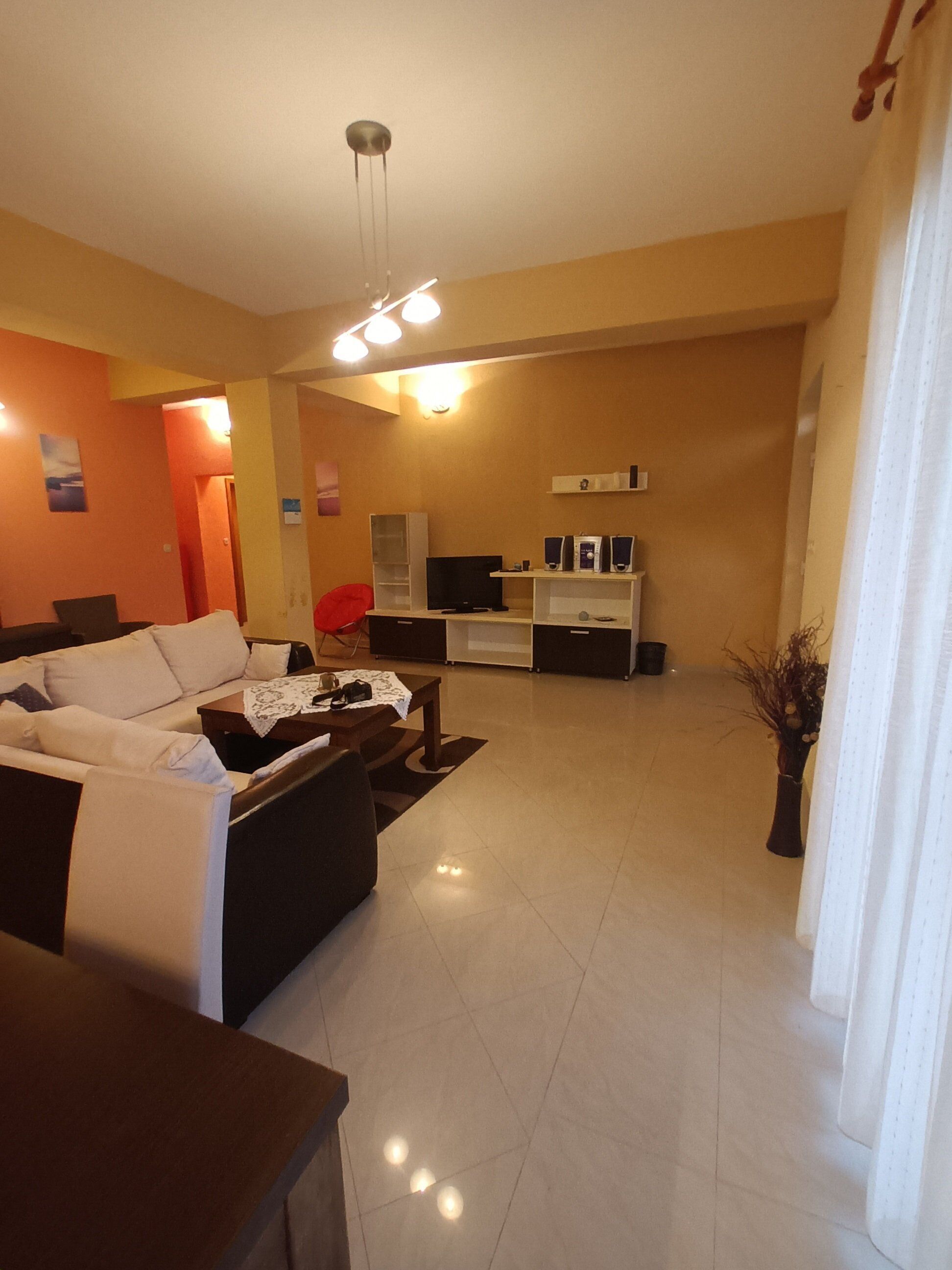 A modern living room with a sofa, a coffee table, a TV, and a small kitchen area with a microwave and a coffee machine.