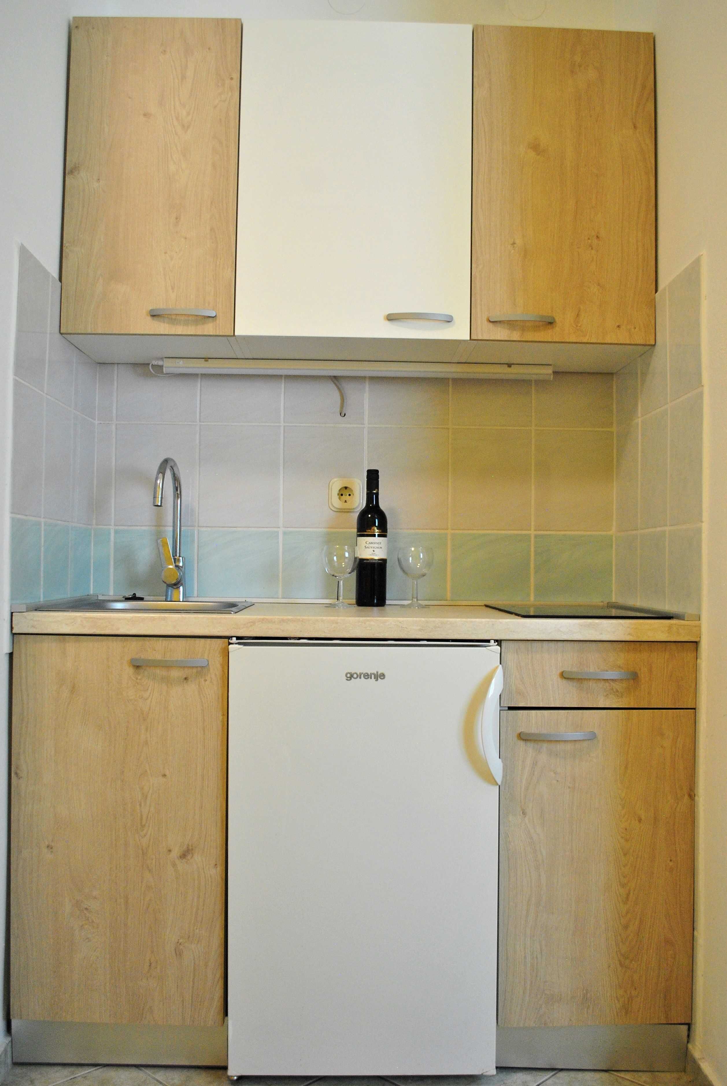 Una cocina con armarios de madera, un refrigerador blanco, un lavabo y una botella de vino.