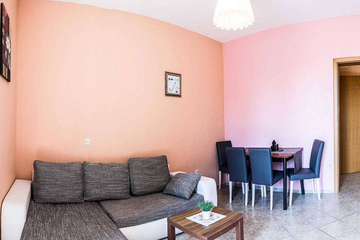A living area with a sofa, a small table with a plant, and a dining table with chairs.