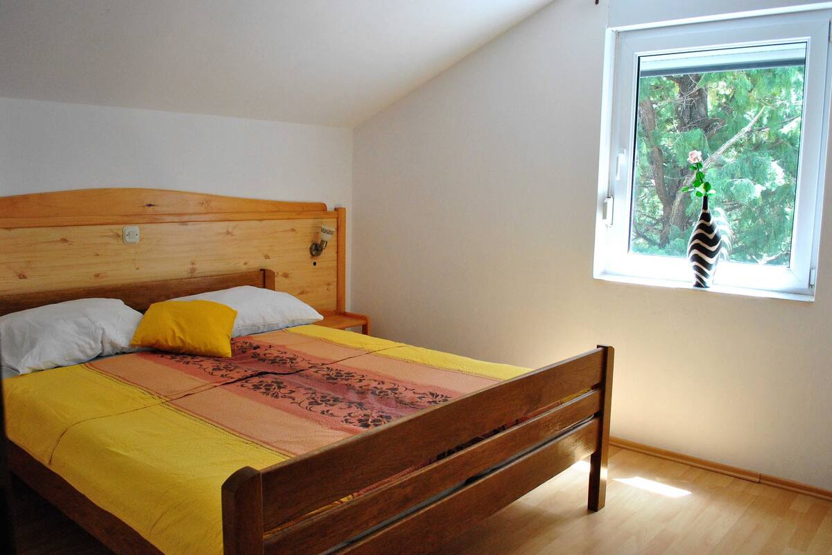 A bedroom with a wooden bed, a window with a view of trees, and a bedside table.