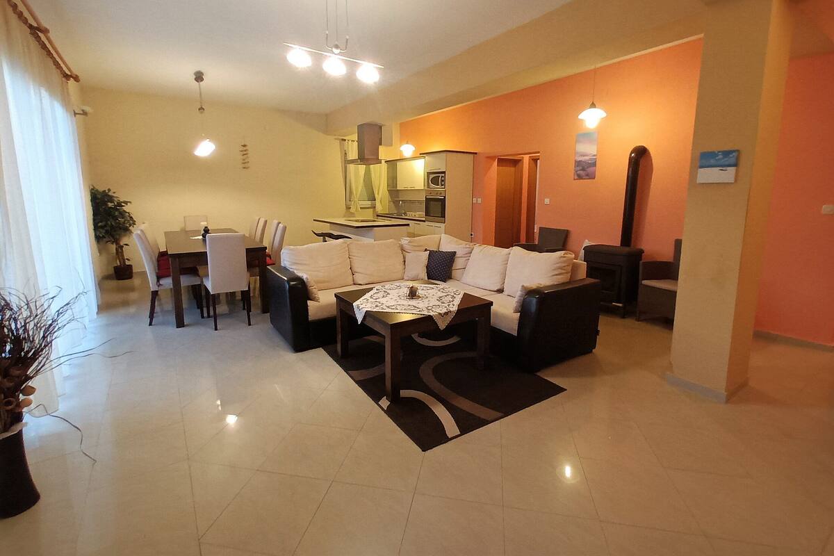 A modern living room with a sofa, coffee table, and dining area. There is a kitchen in the background with a microwave and oven.