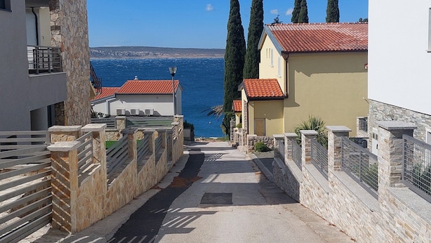 Uma rua estreita com muros de pedra e telhados de telha vermelha, que leva a uma vista do mar.