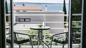 Varanda com duas cadeiras e uma mesa, com vista para um corpo de água e um edifício com telhado de azulejos.