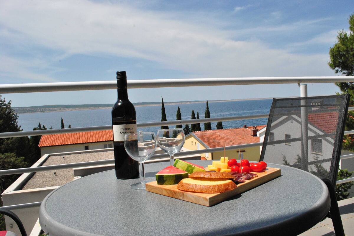 A balcony with a table set for a meal, a bottle of wine, and a view of the sea.