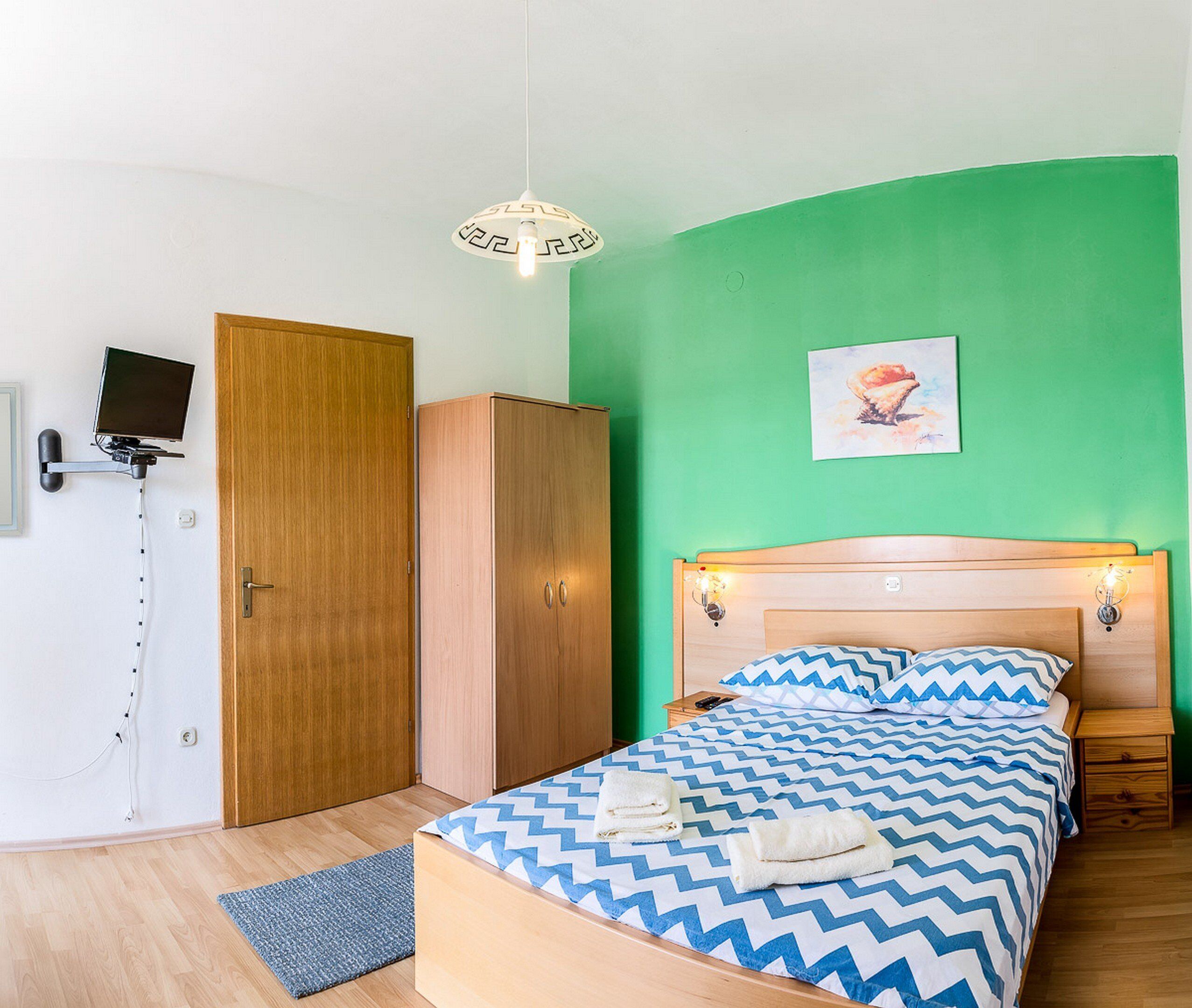 A bedroom with a bed, a wardrobe, a desk, and a television mounted on the wall.