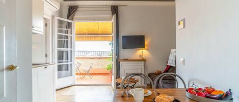 Un comedor con mesa de madera, sillas, televisor montado en la pared y vista al balcón exterior.