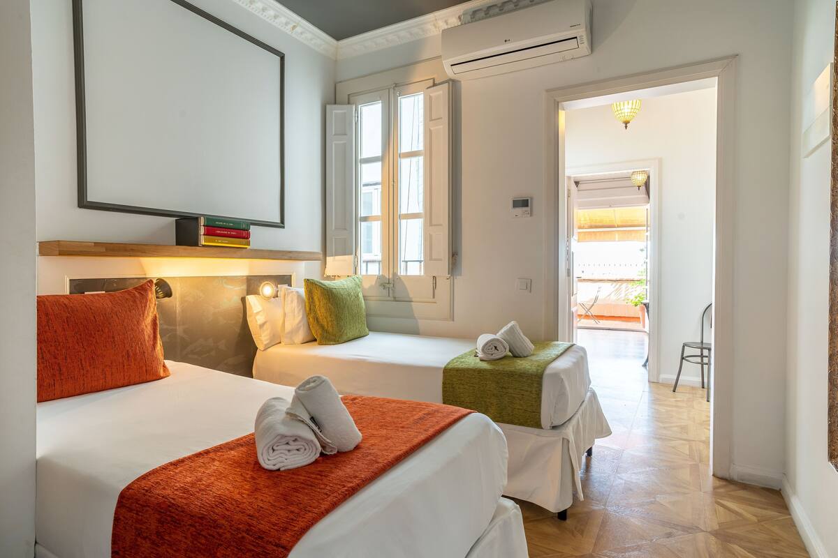 A hotel room with two beds, a large mirror, a flat-screen TV, and a window with shutters.