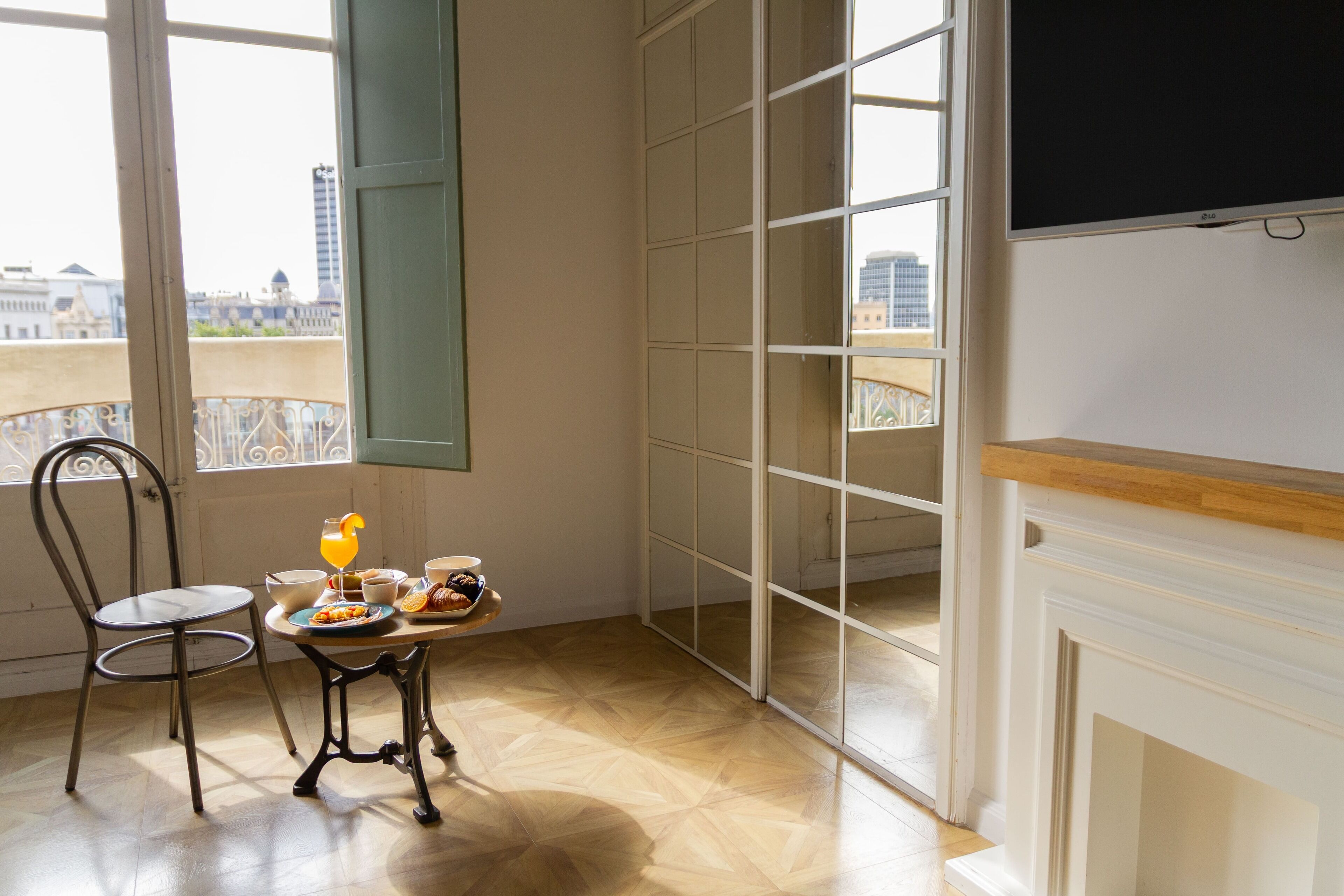 A dining area with a table set for breakfast, a chair, and a view of the city through large windows.