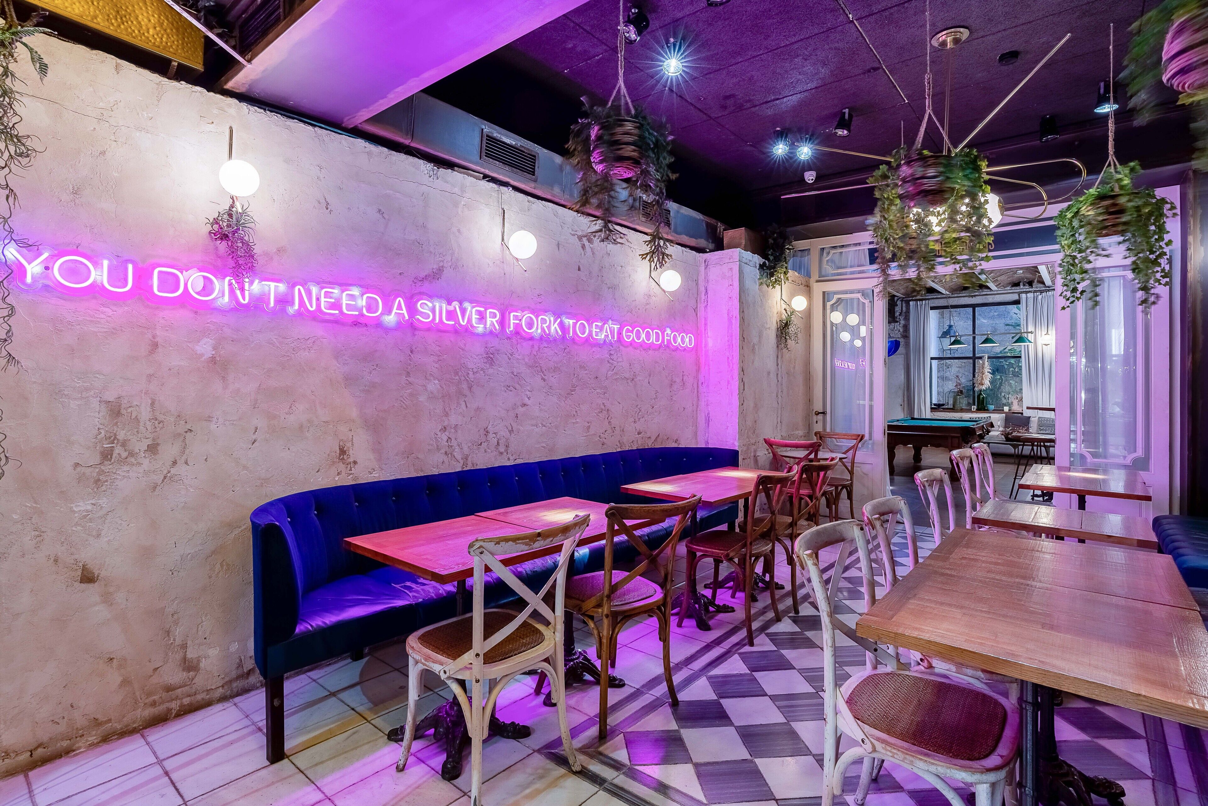 A restaurant interior with a neon sign, wooden tables, and blue seating.