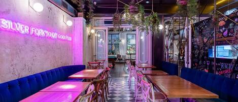 A restaurant interior with neon signage, checkered flooring, and blue upholstered seating.