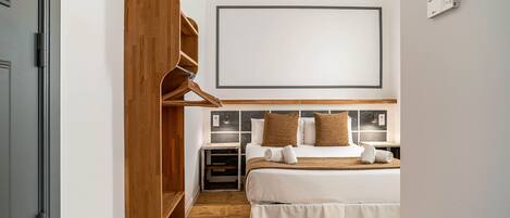 A hotel room with a bed, wooden wardrobe, bedside tables, and a large framed artwork on the wall.