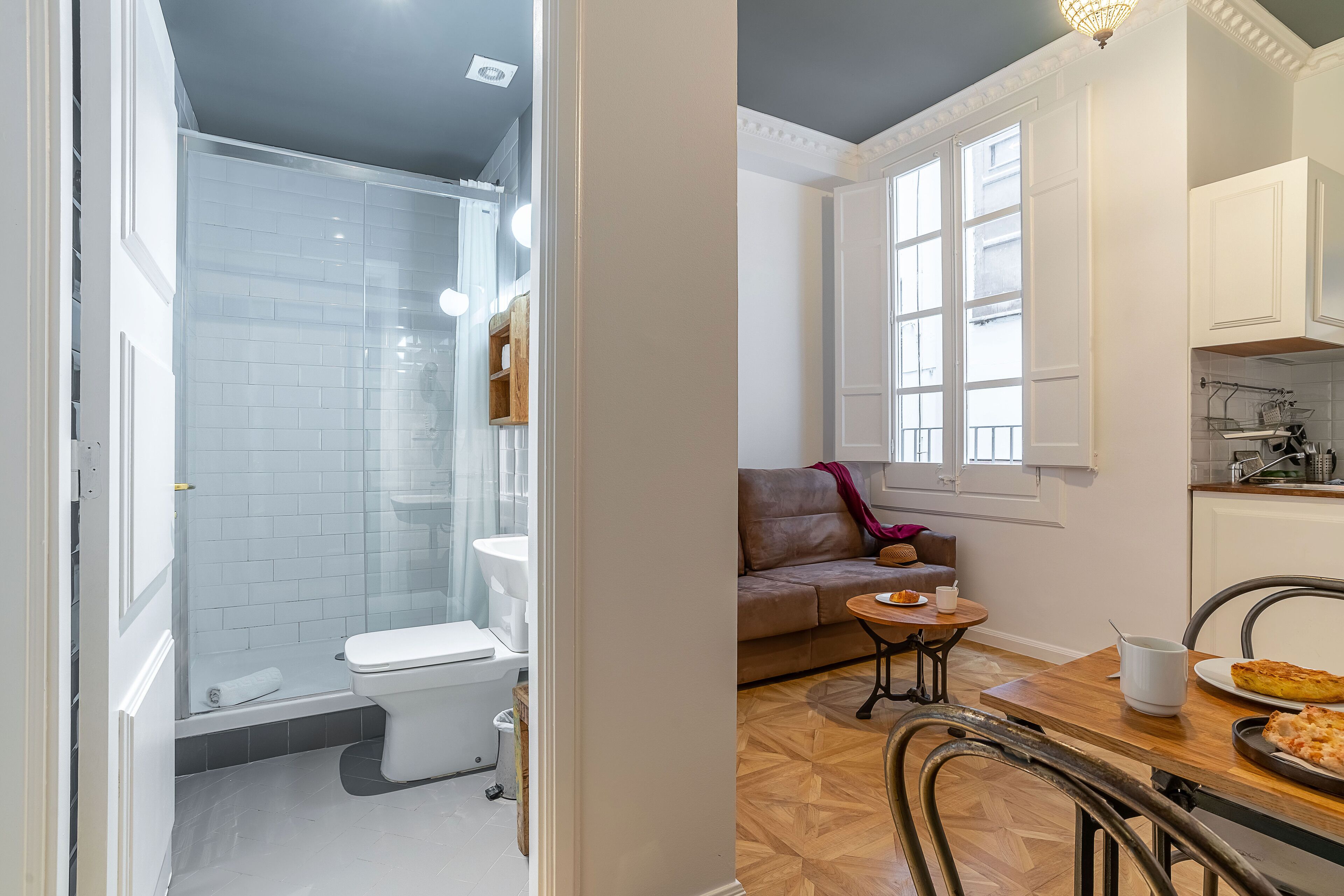 Une salle de bain moderne dotée d’une douche à parois de verre, de toilettes et d’un lavabo. À côté de la salle de bain se trouve un coin repas avec une table en bois, des chaises et un canapé.
