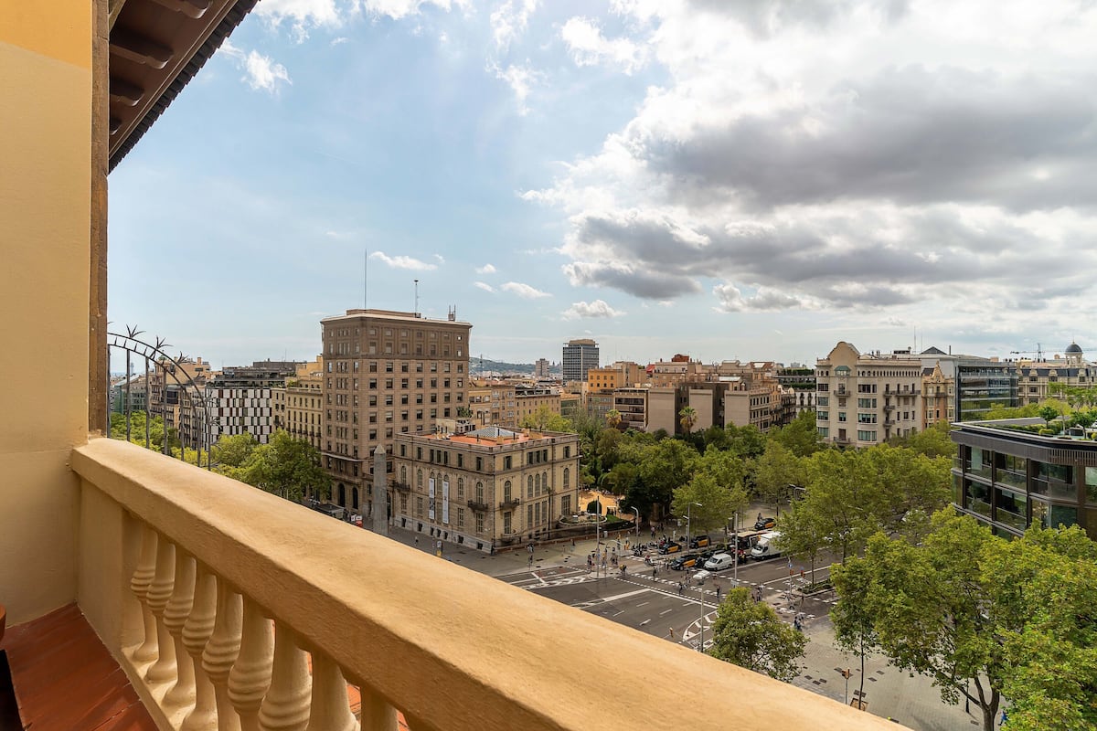 A cityscape with historic buildings and a modern structure, viewed from a balcony with a railing.