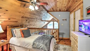 Camera da letto con soffitto in legno, un letto con cuscini, una televisione e una scala che conduce a un livello superiore.