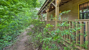 Una baita di legno con un portico, immersa nel verde e raggiungibile tramite un sentiero sterrato.
