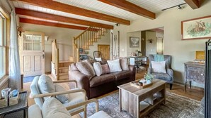 A spacious living room with a brown sofa, a grey armchair, and a wooden coffee table. A staircase leads to an upper level.