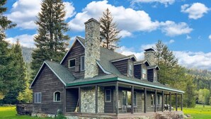 A large, two-story house with a stone chimney, a covered porch, and a well-maintained lawn.