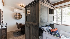 Una camera da letto con un letto a castello in legno, una scrivania e una sedia. Si vede una finestra con vista sugli alberi.