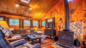 A cozy cabin interior with a leather sofa, a stone fireplace, and a television.
