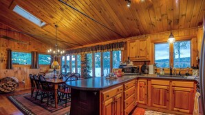 A wooden cabin kitchen with a large island, wooden cabinets, and a view of the forest.
