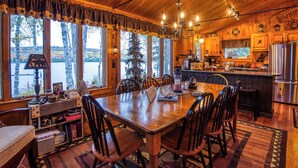A wooden cabin with a dining area, kitchen, and large windows overlooking a lake.