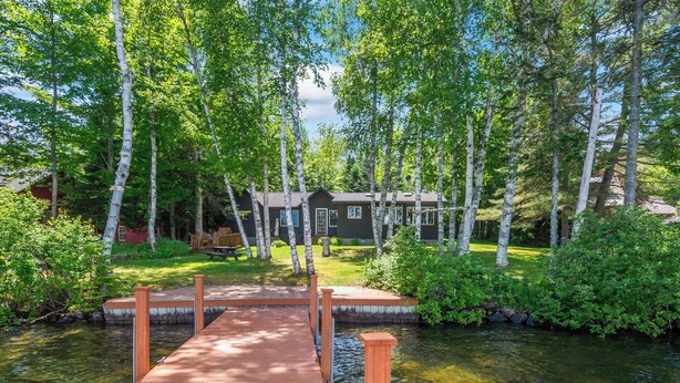A wooden dock leading to a house surrounded by trees.