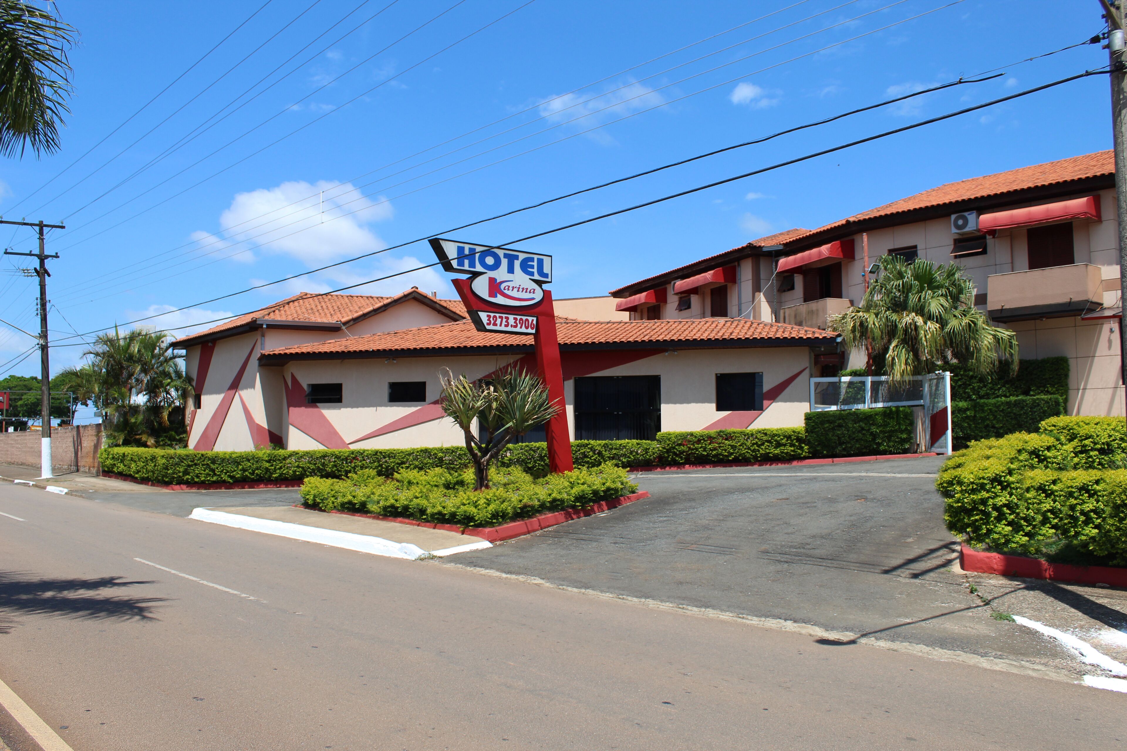 Un hotel con fachada roja y blanca, un letrero llamativo y un jardín bien cuidado.